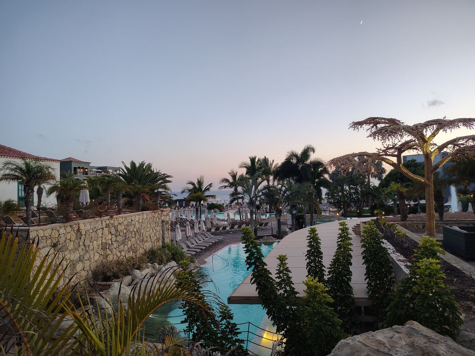 Dusk over the Lopesan Baobab gardens — pools stepping down towards the Atlantic, and a new moon over the whole thing