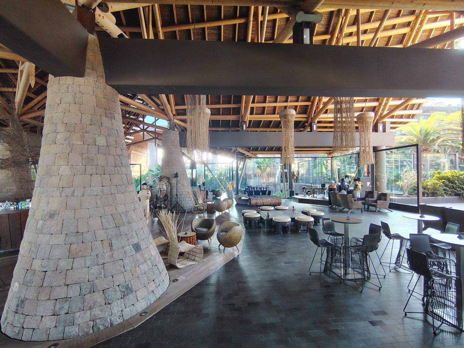 The Lopesan Baobab atrium in daylight — stone chimneys, woven lampshades and a stage at the far end