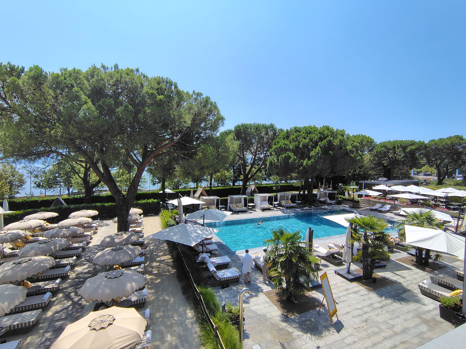 A pool terrace under the umbrella pines at Ouchy, cabanas and all