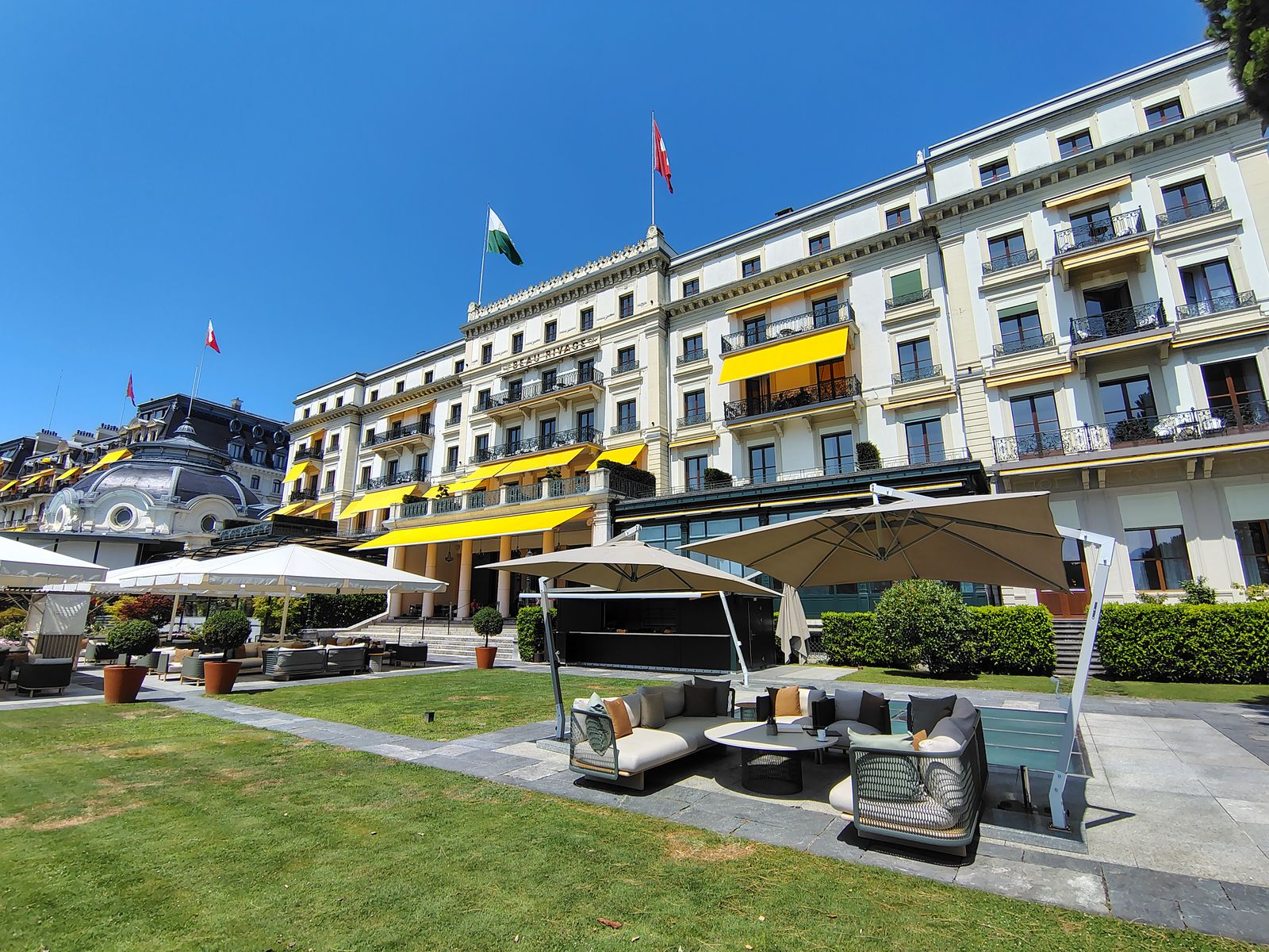 The Beau-Rivage Palace from its own lawn at Ouchy, yellow awnings out against a July sun
