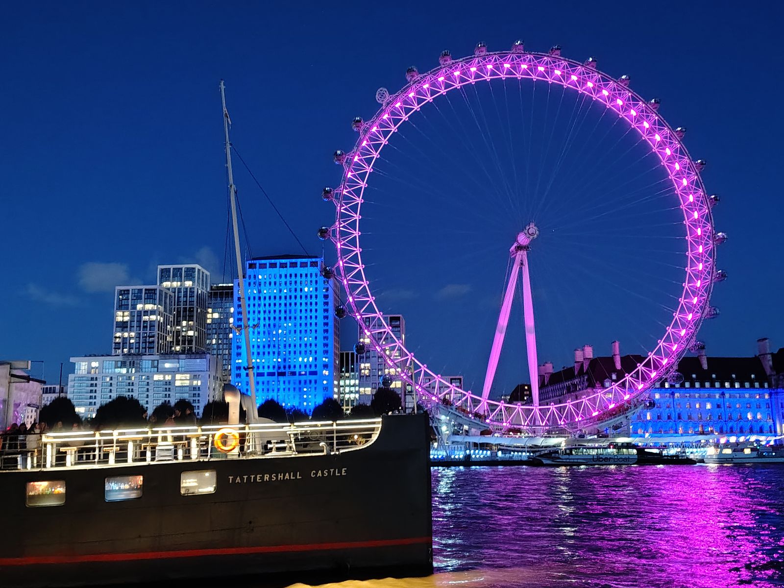 The London Eye lit pink after dark, the Tattershall Castle moored below it