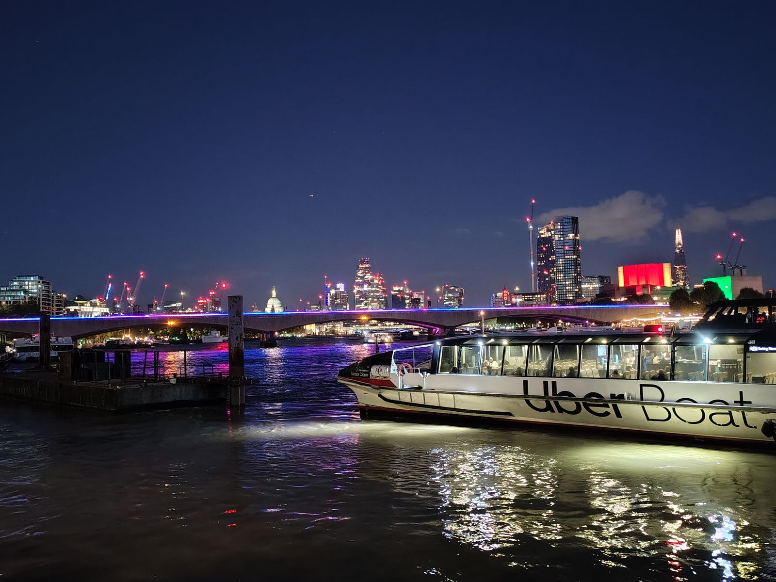 A river bus on the Thames at night, the City and St Paul's lit up behind
