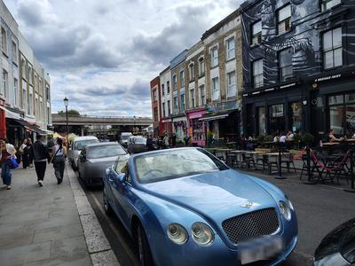 Portobello Road on a summer afternoon, a Bentley convertible parked outside the cafés