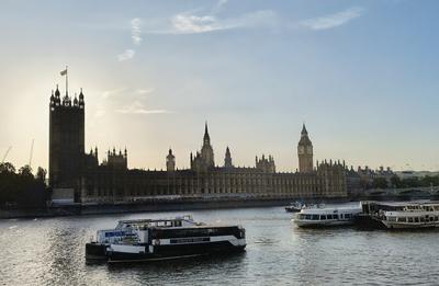The Houses of Parliament from the river on a July evening, a pleasure boat crossing in front — London