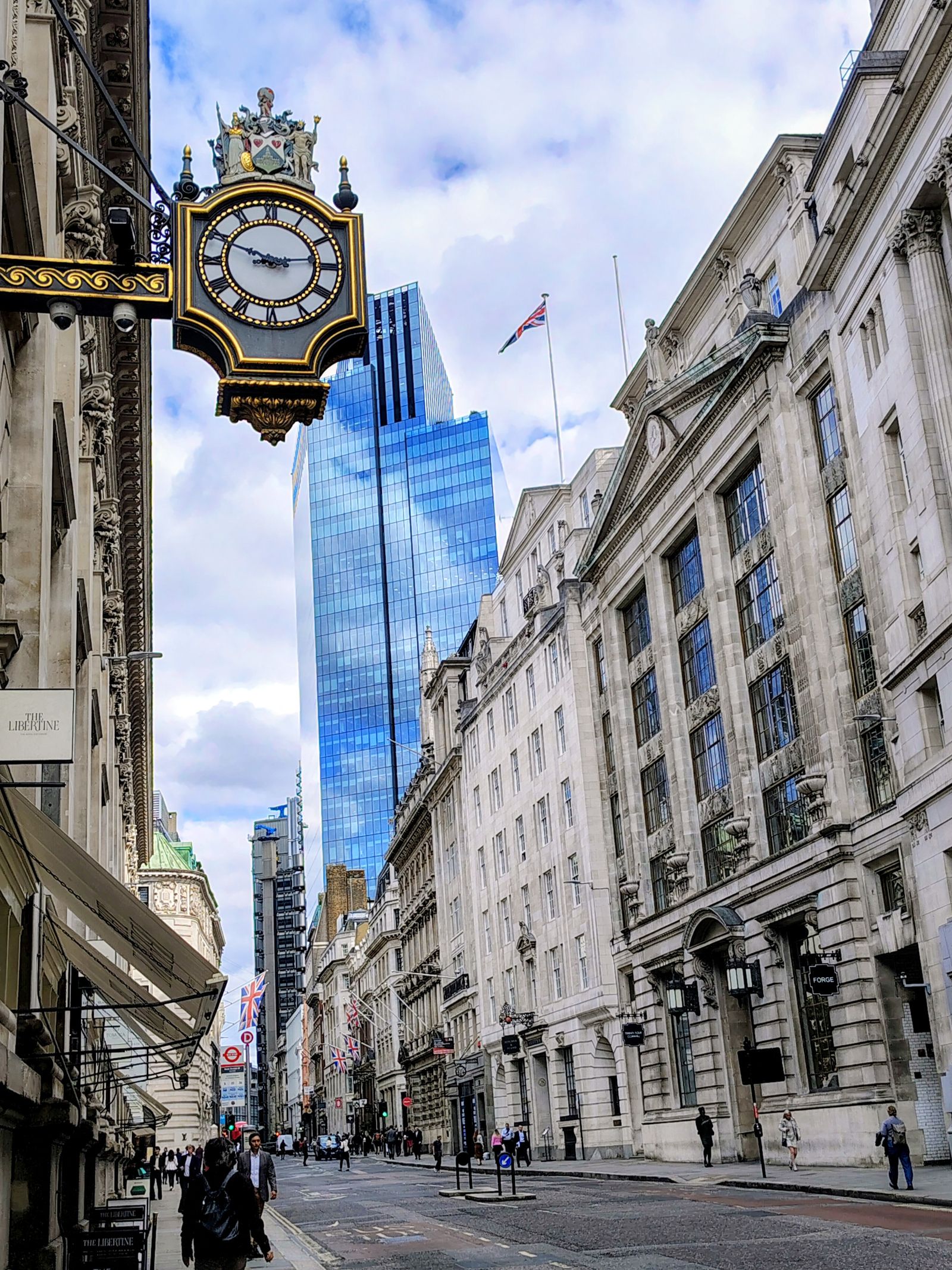 A gilded clock hanging over a City street, the Scalpel rising behind it