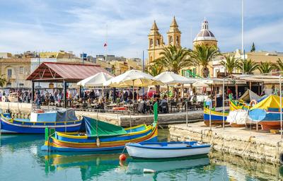 A painted boat under the harbour fortifications — Malta