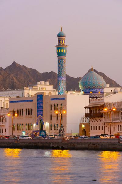 A blue-tiled dome and banded minaret above the water — Oman